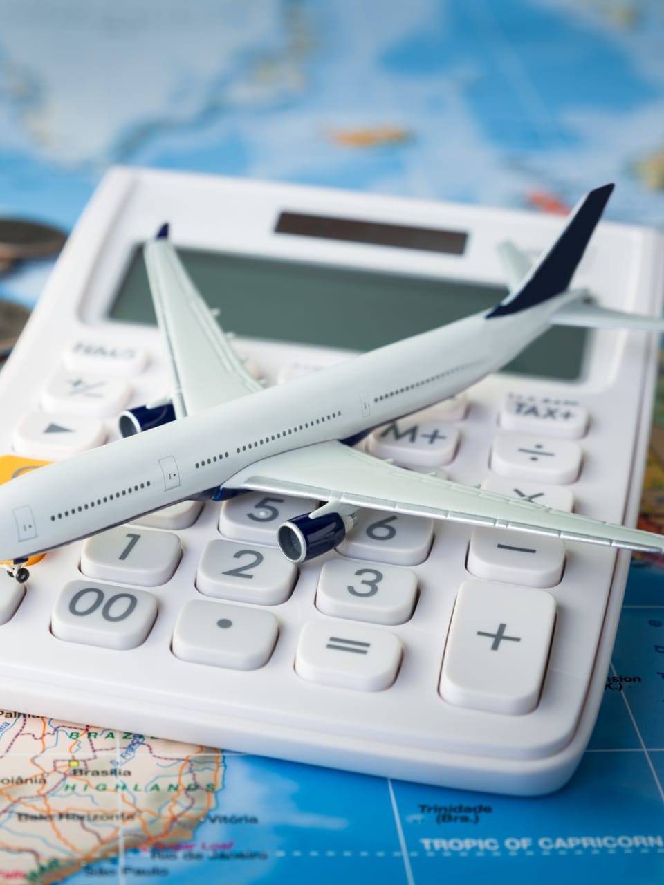 Flugzeug auf einem Taschnerechner mit Kleingeld auf einer Weltkarte © iStock.com/Sezeryadigar