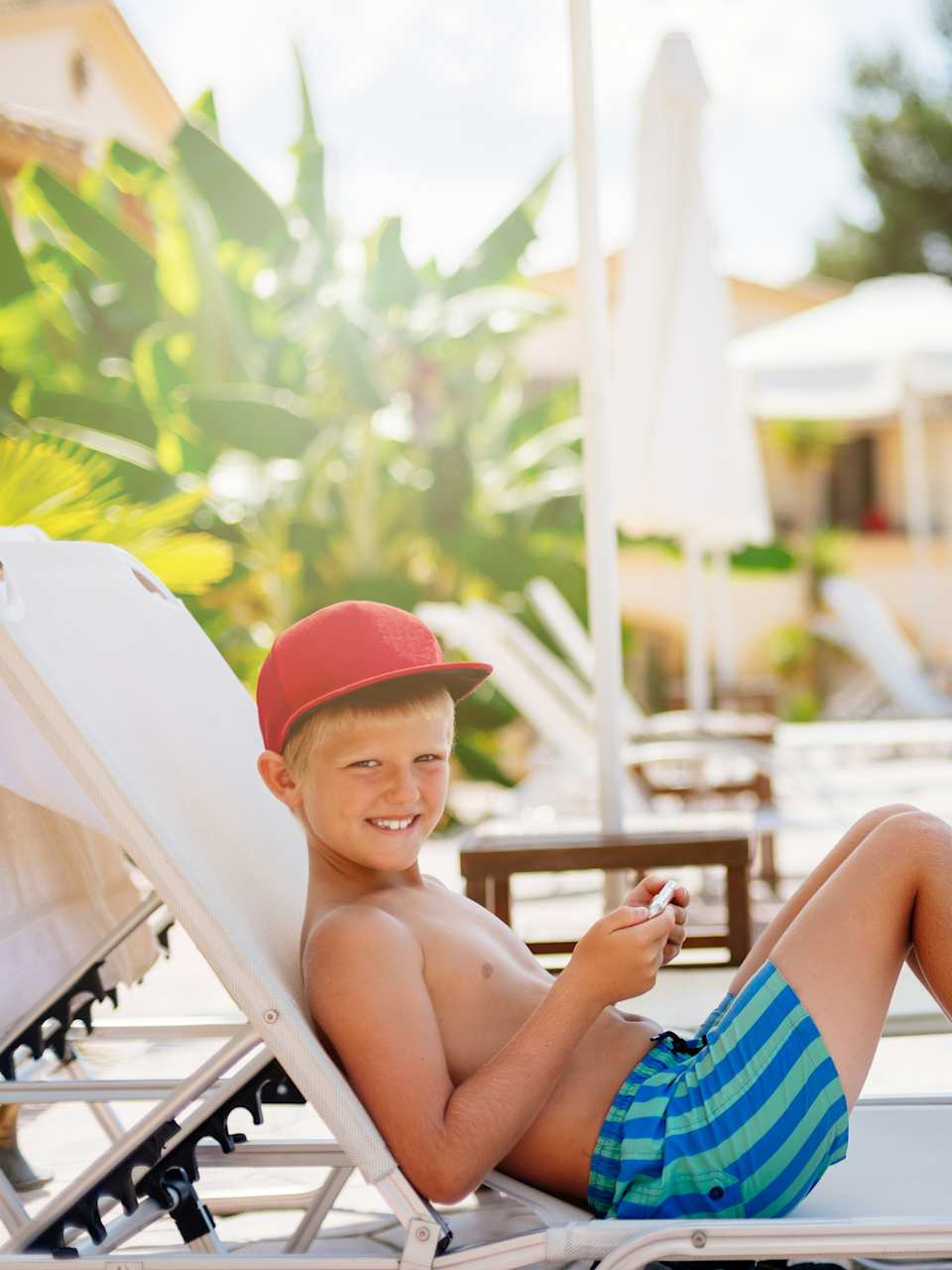 Junge in Badehose entspannt sich glücklich auf einer Sonnenliege am Pool ©iStock.com/djedzura