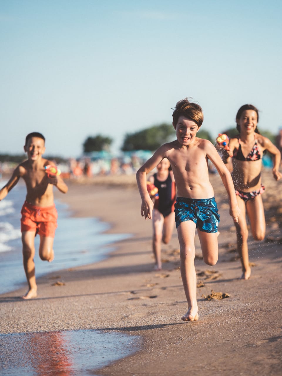 Kinder laufen und schießen mit Wasserpistolen am Strand © iStock.com/martin-dm