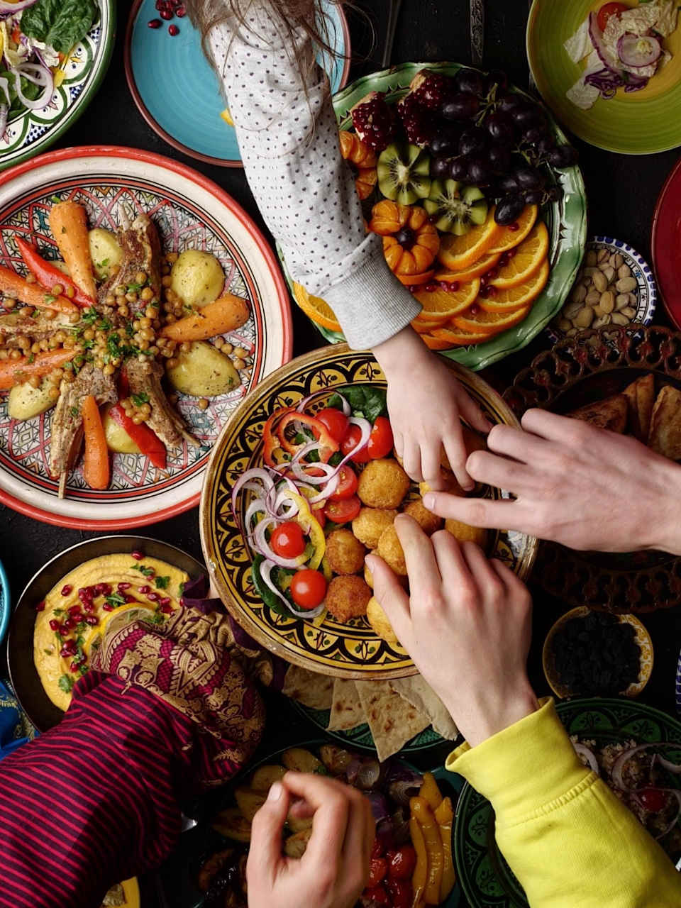 Blick von oben auf eine Vielzahl von Gerichten, mehrere Hände greifen nach Essen