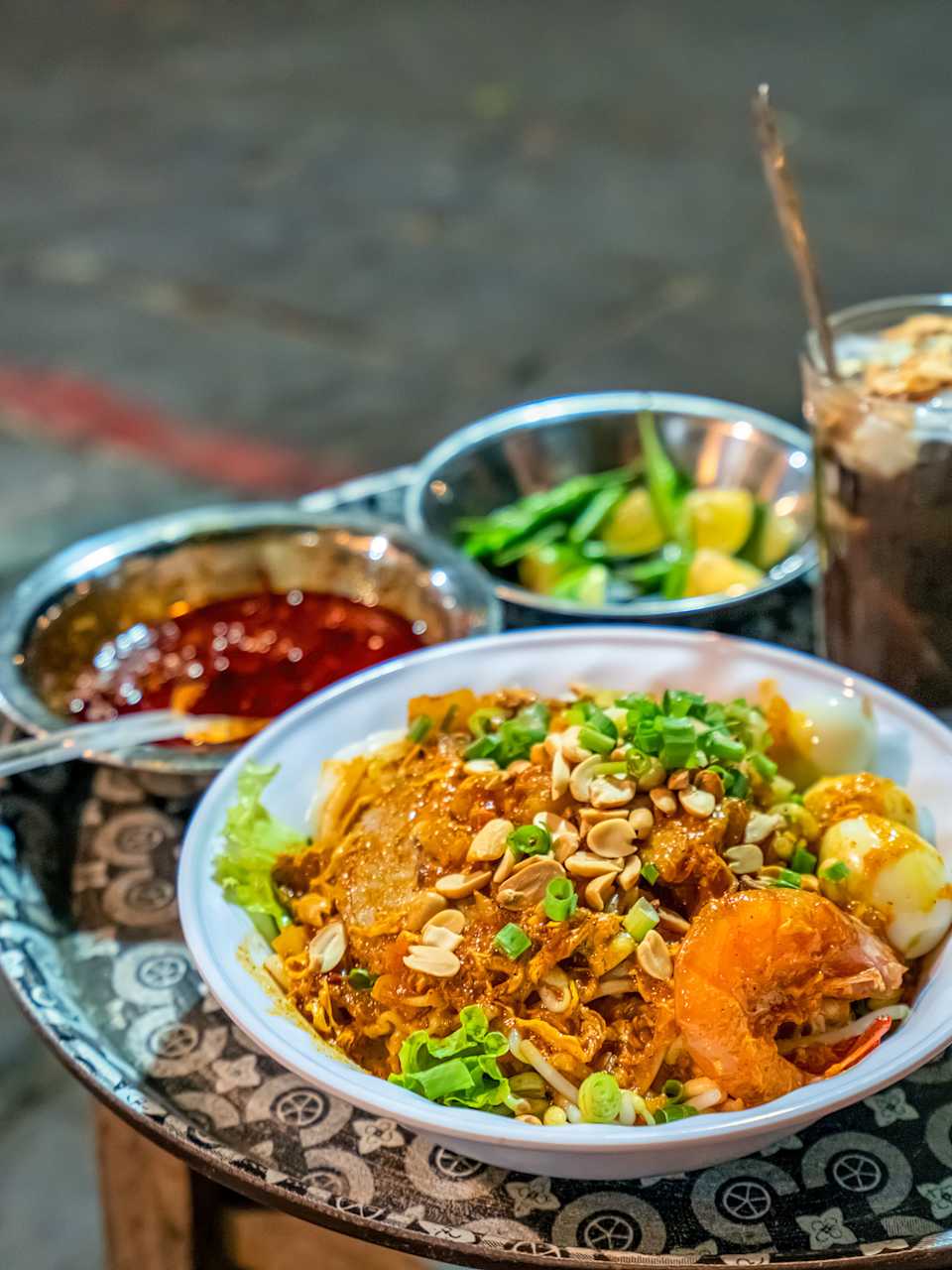 Auf einem kleinen Beistelltisch steht ein Teller vietnamesisches Mi Quảng, eine Soße und Getränke.