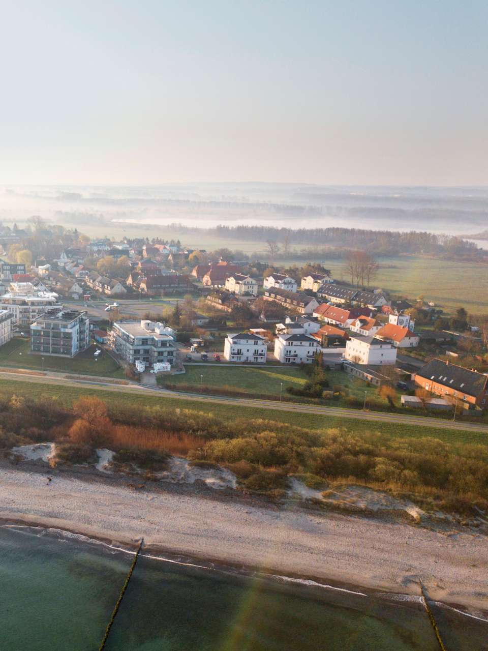Drohnenaufnahme Strand und Städtchen im Nebel von oben.