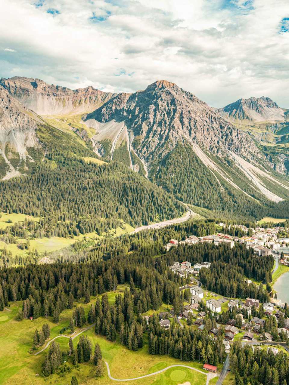 Luftaufnahme des Obersees in Arosa mit umliegendem Bergpanorama, Nadelwäldern und der Ortschaft am Fuße der Graubündner Alpen