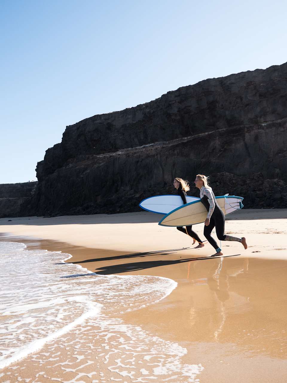 Surferinnen am Strandufer rennen zu den Wellen © iStock.com/1MEDIA