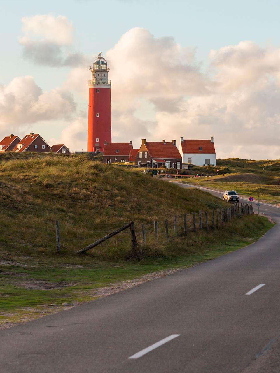 Autos und Fußgänger auf einer Straße zu einem Leuchtturm in Nordholland, Niederlande.