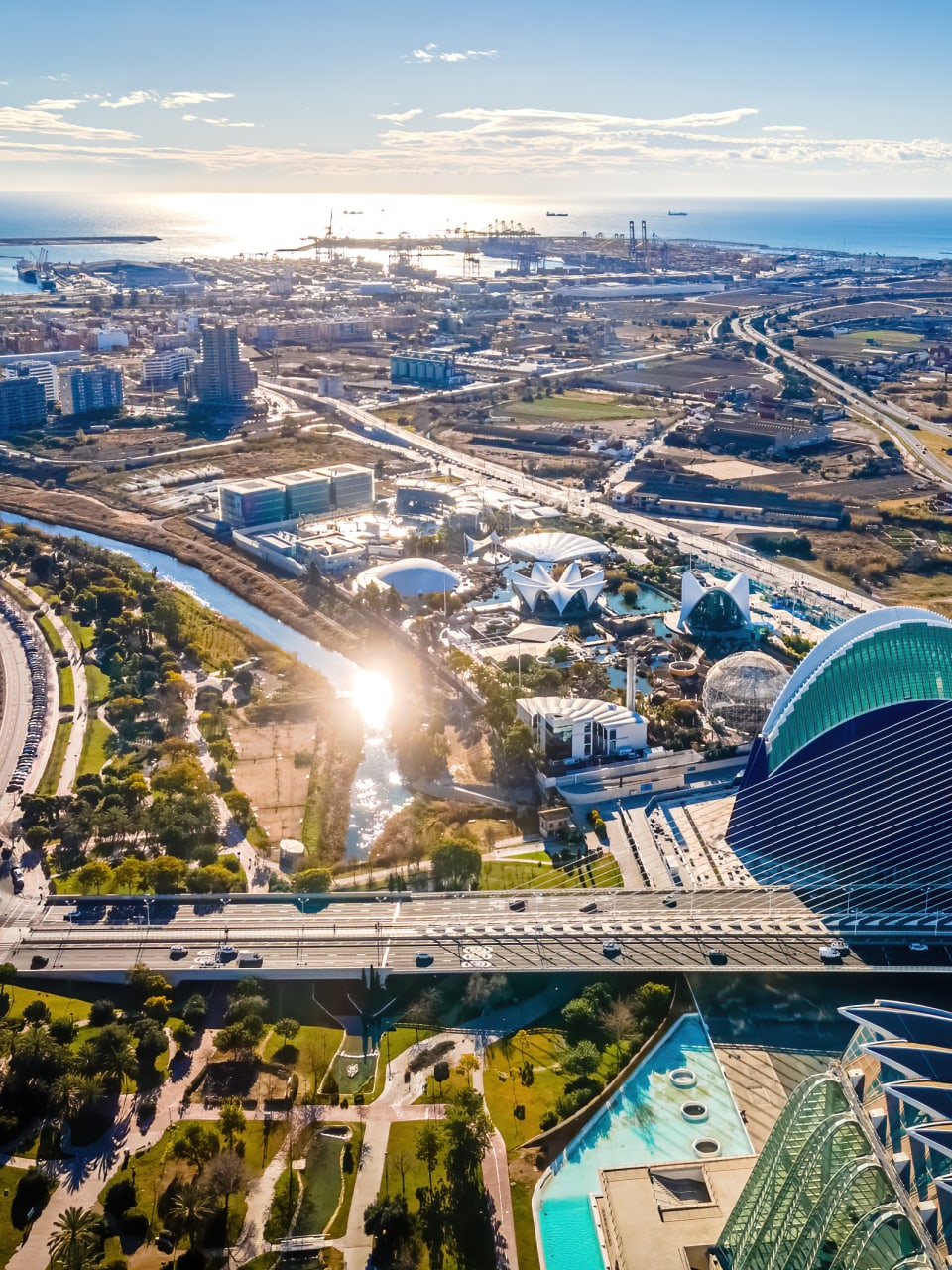 Drohnenfoto über die außergewöhnlich geformten Gebäude der Ciudad de las Artes y Sciencias. Das Viertel hat viele Grünanlagen. In der Ferne sieht man das Meer