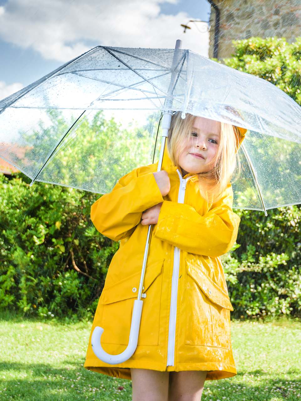 Ein Mädchen mit einem gelben Regenmantel unter einem Regenschirm.