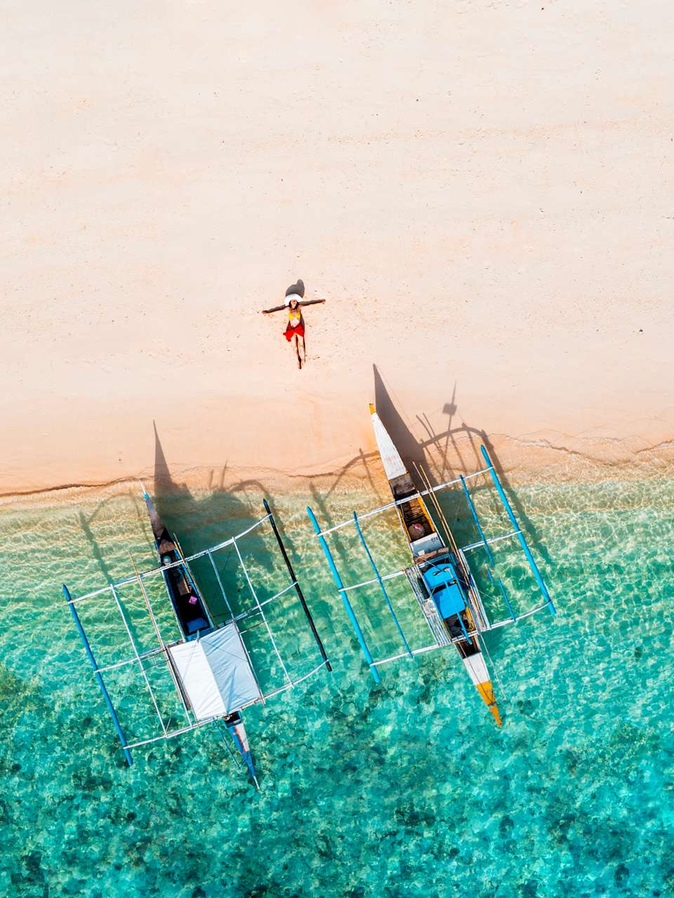 Eine Frau liegt neben zwei Booten an einem Strand auf den Philippinen. © Marco Bottigelli/Moment via Getty Images