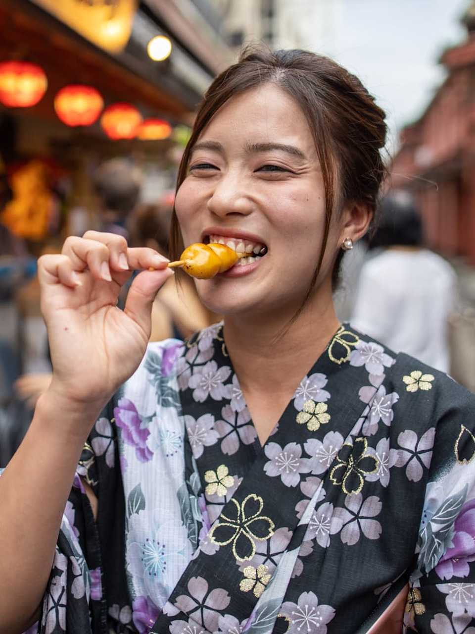 Eine junge Frau ist Dango Knödeln auf der Straße in Tokyo.