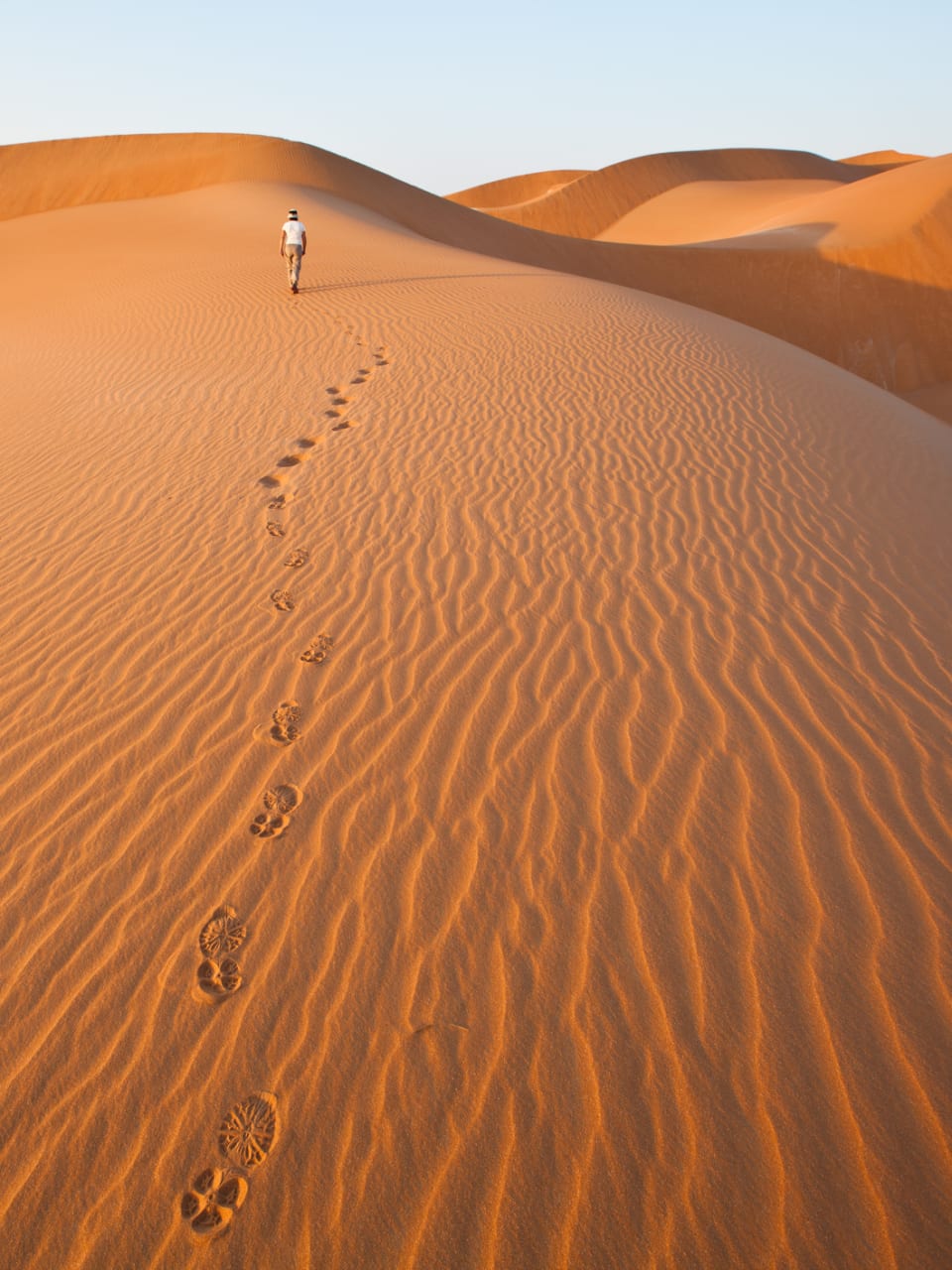 Eine Person läuft durch die Wüste und hinterlässt Fußspuren im Sand.