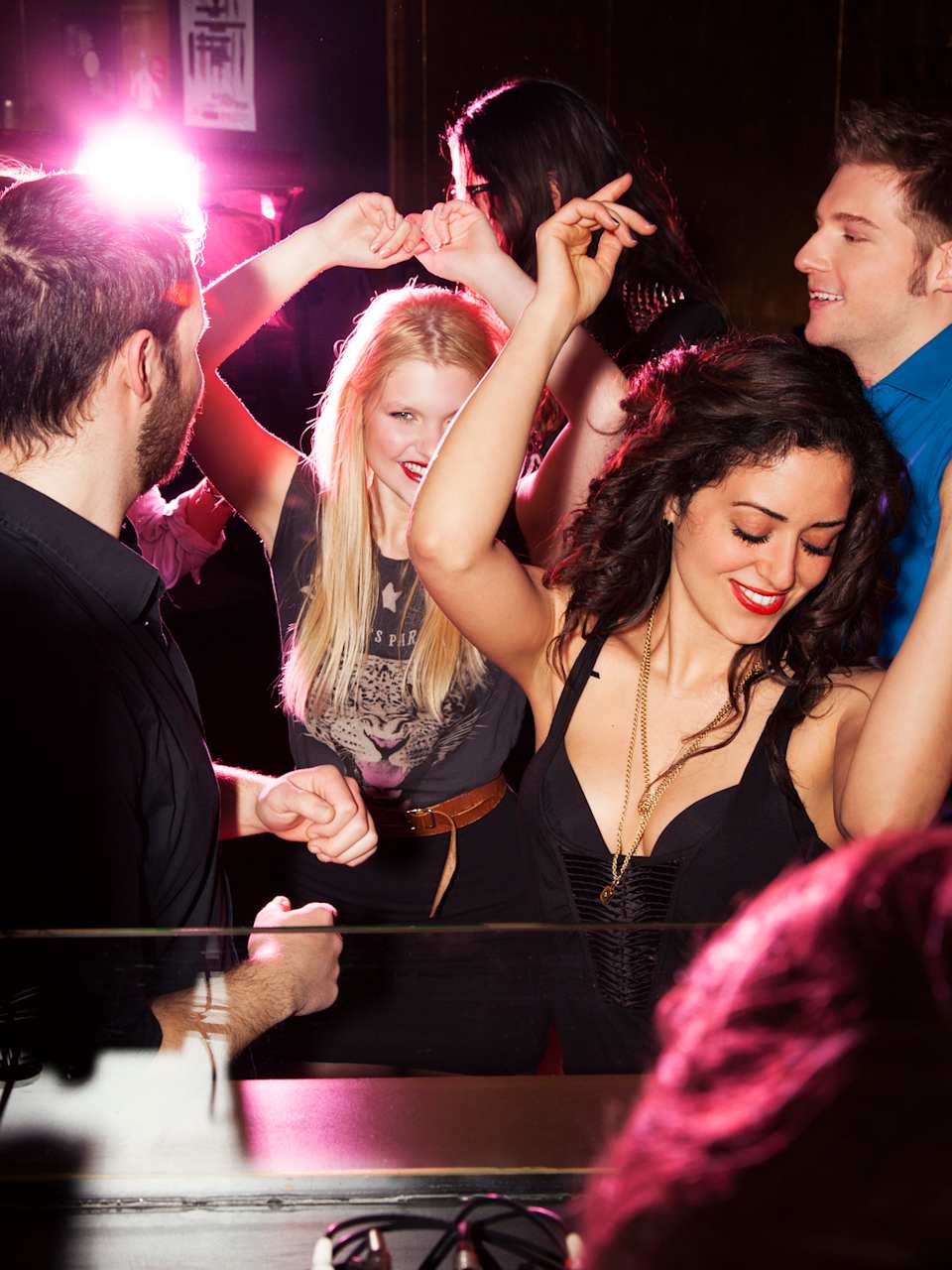 Gruppe von Freunden tanzt vor dem DJ-Pult in Nachtclub. © Manuela/Image Source via Getty Images