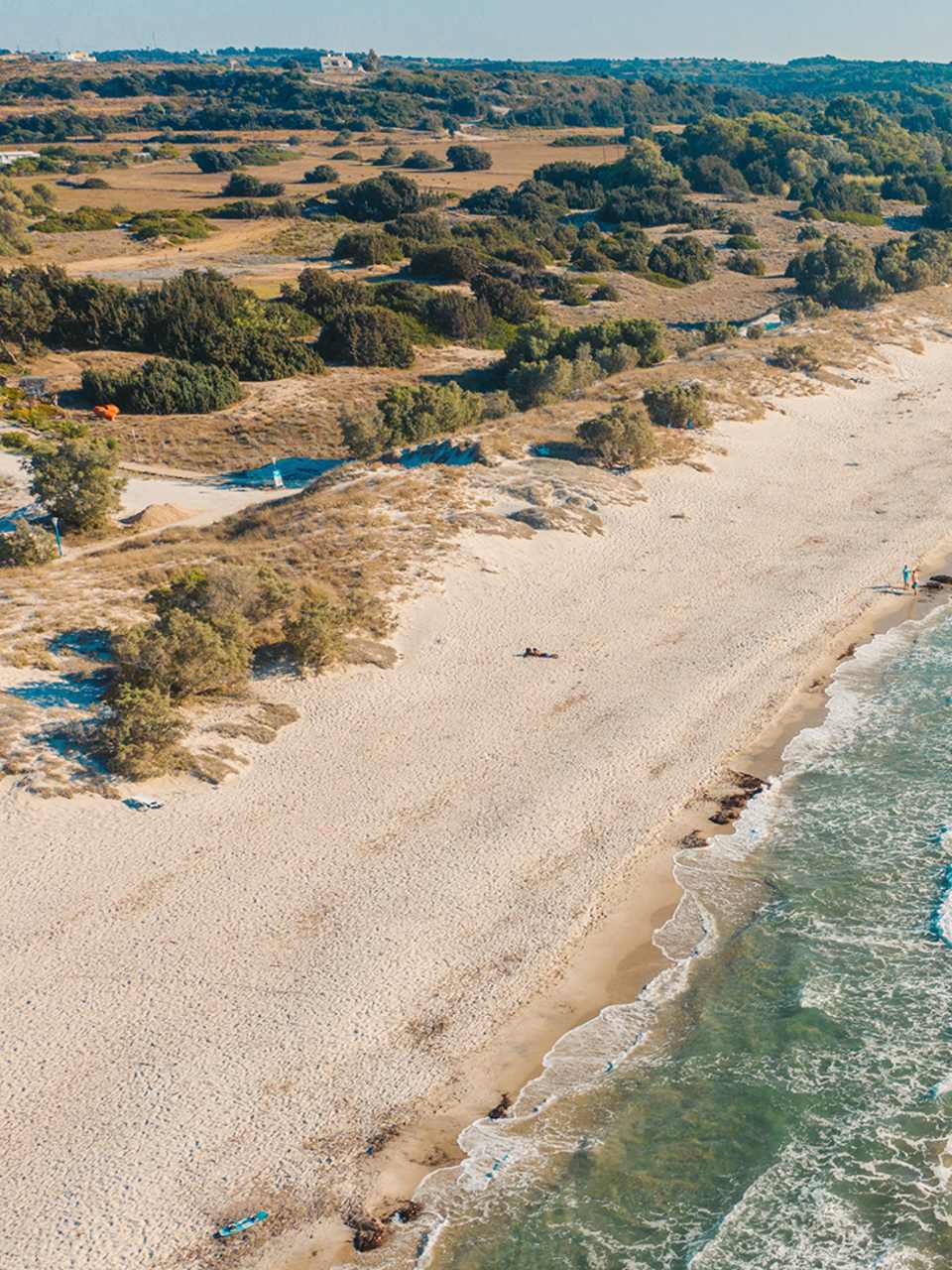 Ein langer Sandstrand in einer ländlichen Umgebung, der von Kitesurfern genutzt wird