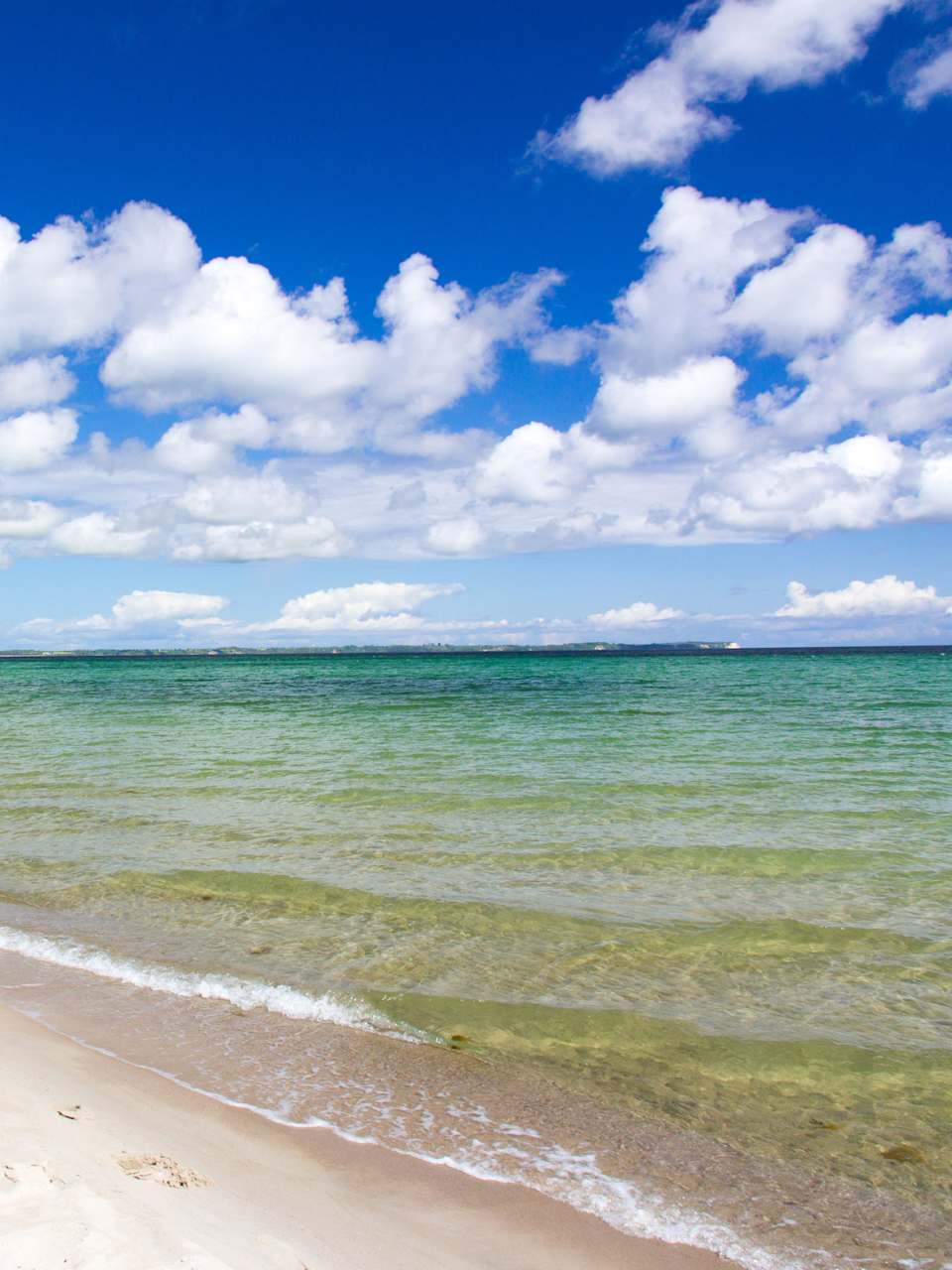 Ein langer leerer Strandabschnitt. In der Ferne spazieren zwei Menschen