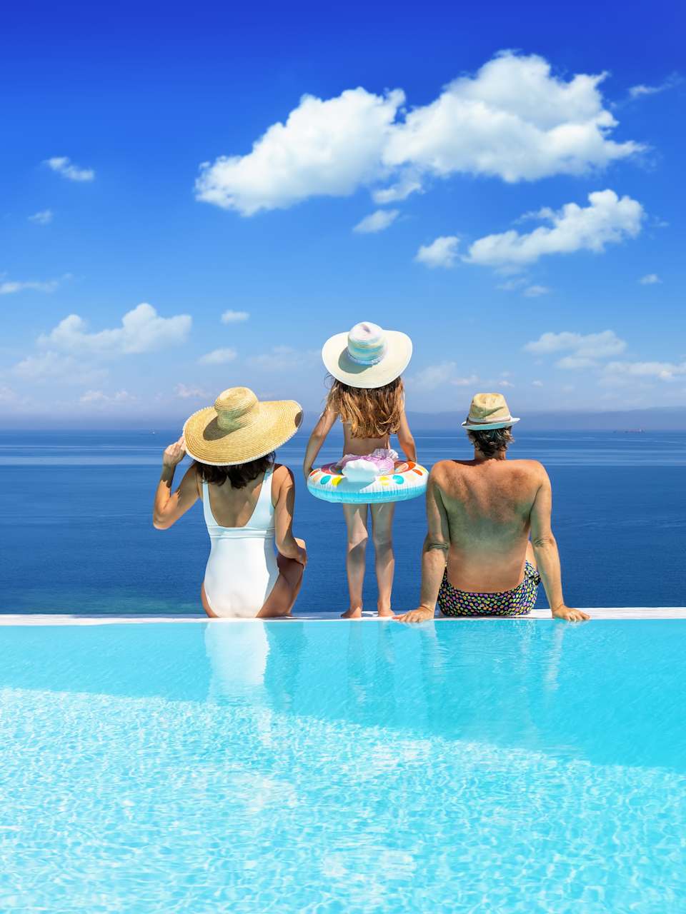 Familie sitzt am Pool mit Blick aus Meer