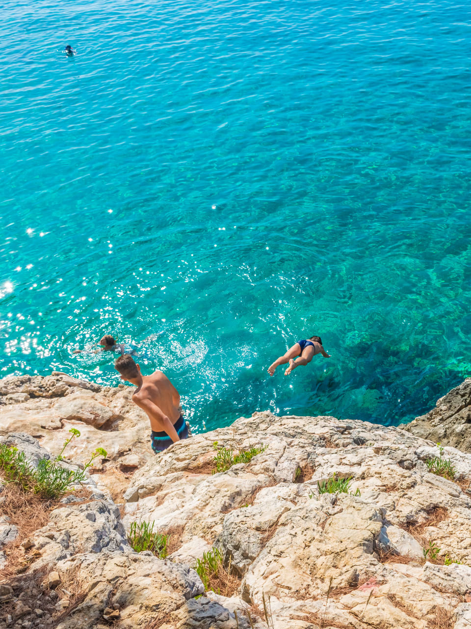 Kinder springen ins Meer von Klippen am Jagodna Beach auf der Insel Hvar, Kroatien