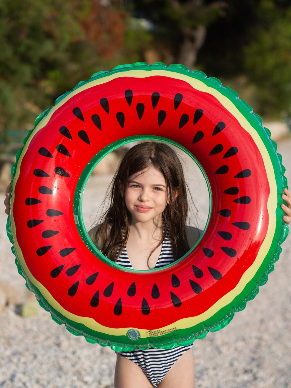 Mädchen hält einen Schwimmring in Melonen-Optik an einem Strand in Kroatien hoch.