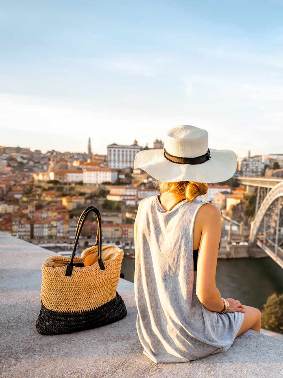 Frau mit Hut sitzt mit Blick auf eine Brücke in Porto