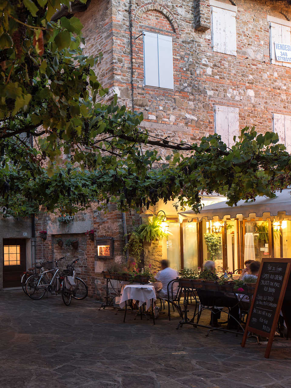 Altstadtgassen  mit großem Baum und Restaurant in Grado am Abend