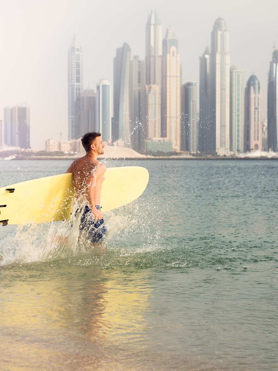 Surfer läuft ins Wasser vor der Hochhaus-Kulisse von Dubai.