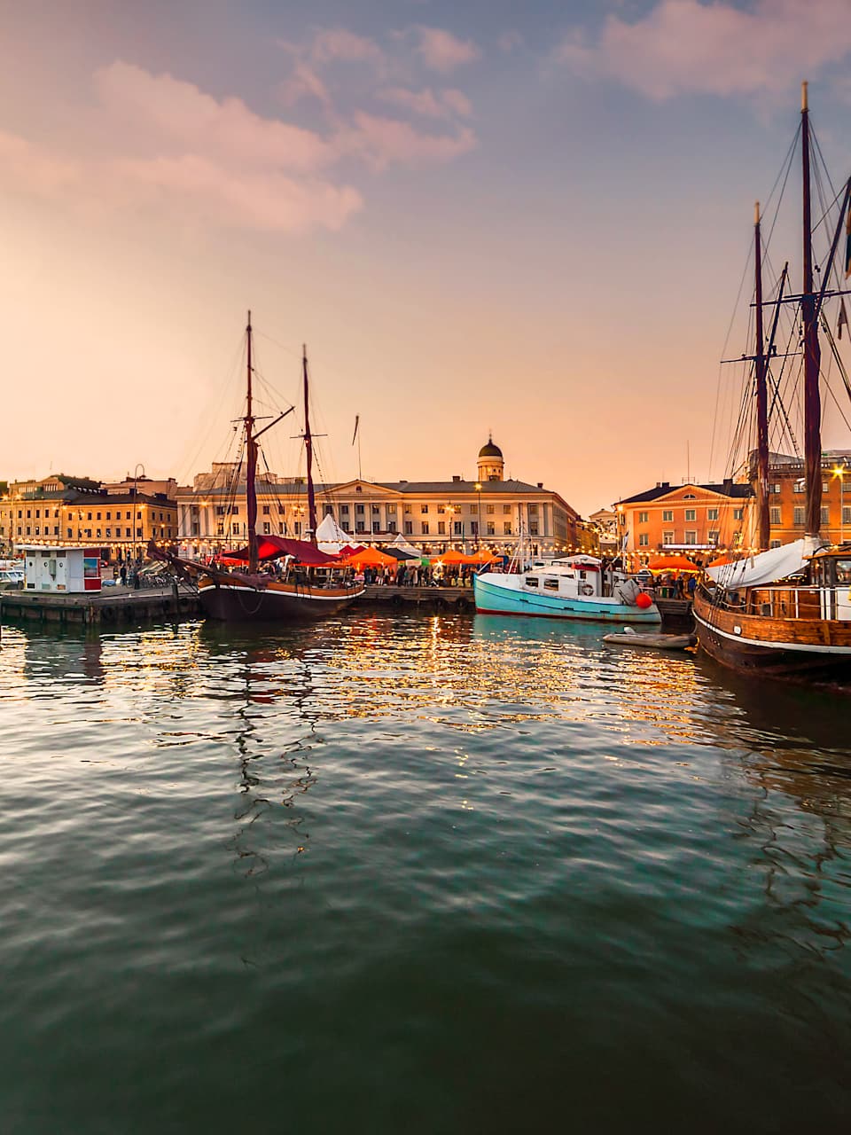 Ein Hafen bei Sonnenuntergang. Mehrere Boote liegen im ruhigen Wasser, die Promenade ist mit Lichterketten dekoriert.