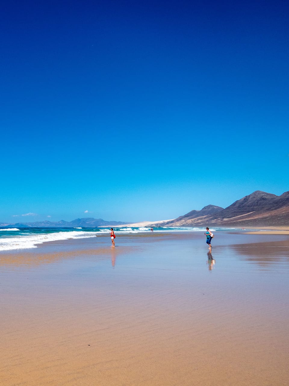 Ein weiter Strand mit tiefblauem, wolkenlosem Himmel und Bergen im Hintergrund.