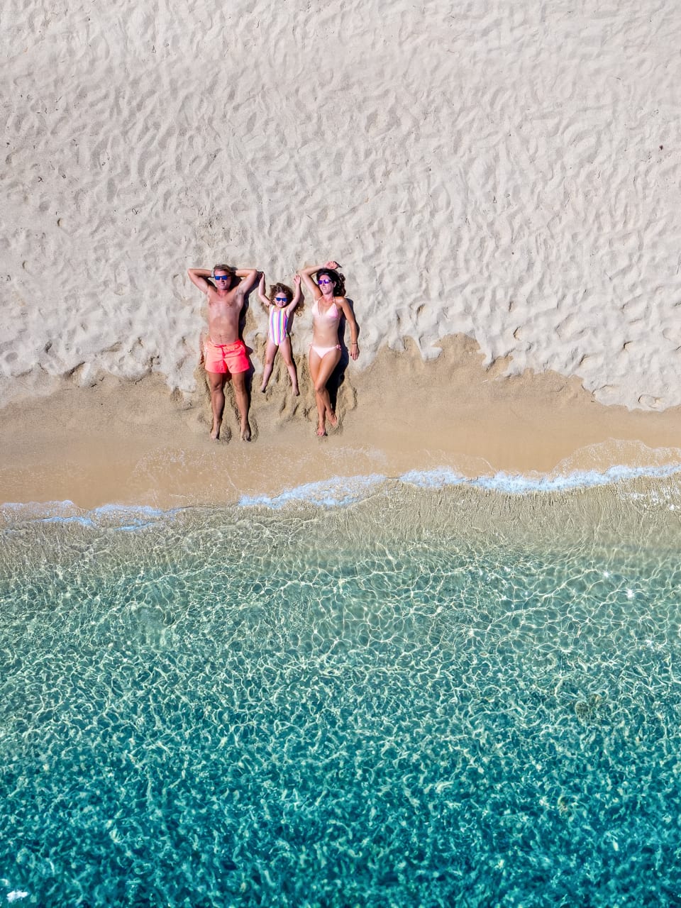Vater, Mutter und Kind liegen an einem Strand am Meer.