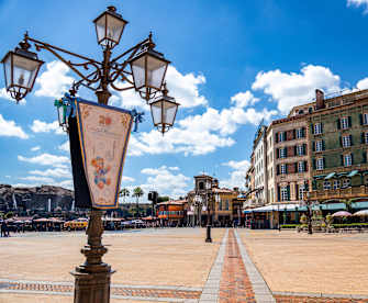 Ein Platz mit bunten, ästhetischen Häusern am Rand, einer verschnörkelten Laterne im Vordergrund und im Hintergrund Berge mit kleinen Wasserfällen im DisneySea bei Tokyo, Japan.