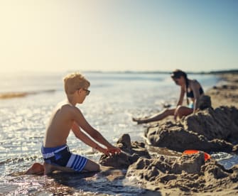 Kinder spielen am Strand und bauen eine Sandburg © iStock.com/Imgorthand