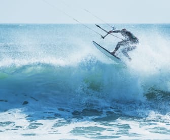Kitesurfer springt über eine schäumende Welle © iStock.com/shaunl