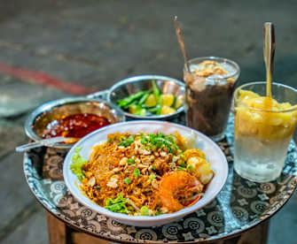 Auf einem kleinen Beistelltisch steht ein Teller vietnamesisches Mi Quảng, eine Soße und Getränke.