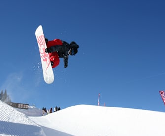 Snowboarder in der Luft beim Trick über einen Kicker im Funpark, blauer Himmel im Hintergrund, Avoriaz, Schweiz.