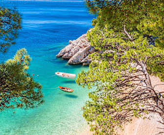 Idyllischer Strand Punta Rata in Brela mit Blick durch mediterrane Bäume, Kroatien. © xbrchx via Getty Images