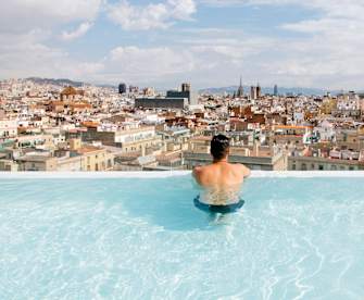 Ein Mann schaut aus einem Infinity Pool über Barcelona, Spanien.