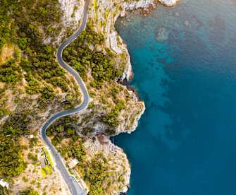 Dronenblick auf die Küstenstraße und tiefblaues Meer an der Amalfiküste, Italien. © Marco Bottigelli via Getty Images