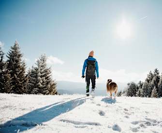 Eine Frau wandert mit ihrem Hund in einer verschneiten Landschaft.