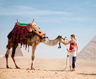 Mutter und Sohn streicheln ein Kamel in der Wüste.