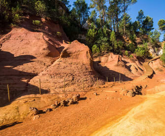 Ein ockerfarbener Wanderweg mit Bäumen im Hintergrund in Roussillon in Frankreich.