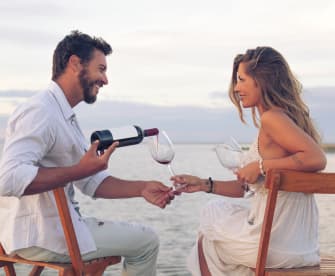 Paar am Strand, Mann gießt Wein in ein Glas ein in Griechenland