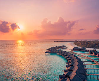 Sonnenuntergang im Meer neben Wasservillen und Holzsteg, Malediven. © Levente Bodo via Getty Images