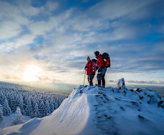 Zwei Wanderer stehen auf einem schneebedeckten Gipfel.