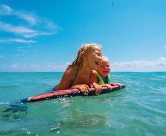 Zwei Kinder schwimmen mit einem Schwimmbrett im Meer.