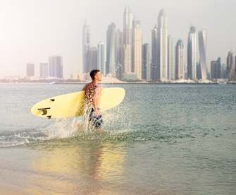 Surfer läuft ins Wasser vor der Hochhaus-Kulisse von Dubai.