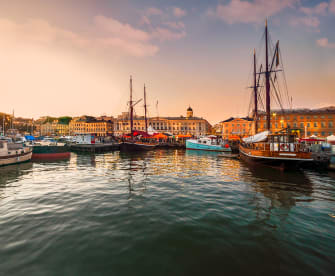 Ein Hafen bei Sonnenuntergang. Mehrere Boote liegen im ruhigen Wasser, die Promenade ist mit Lichterketten dekoriert.