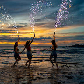Drei Frauen springen ins Meer mit Silvesterfontänen und haben Spaß