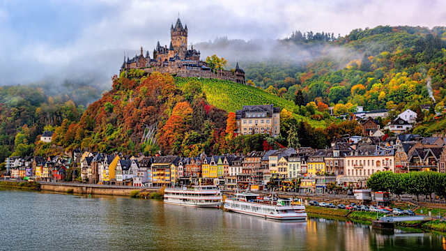 Blick auf eine kleine Stadt am Fluss mit einer Burg auf einem Berg