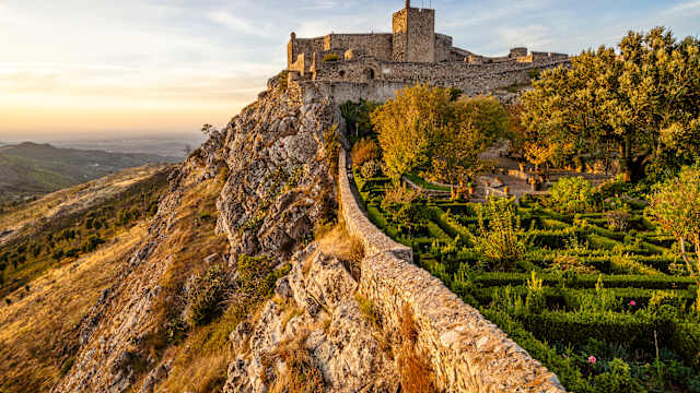 Eine mittelalterliche Burg liegt auf einem Berg und wird vom Sonnenuntergang angeschienen.