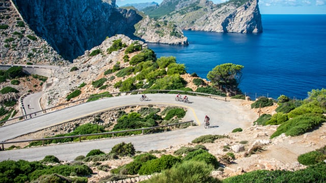 RadfahrerInnen fahren eine Straße mit Meerblick entlang auf Mallorca, Spanien.