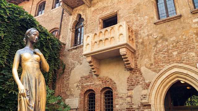Eine Statue einer Frau steht unter dem Balkon eines alten Hauses.