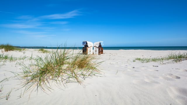 Zwei Strandkörbe stehen an einem leeren Strand.