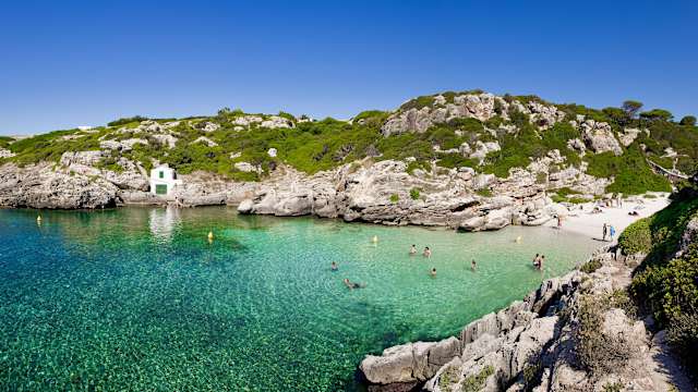 Bucht auf Menorca mit grünblauem Wasser und Badegästen